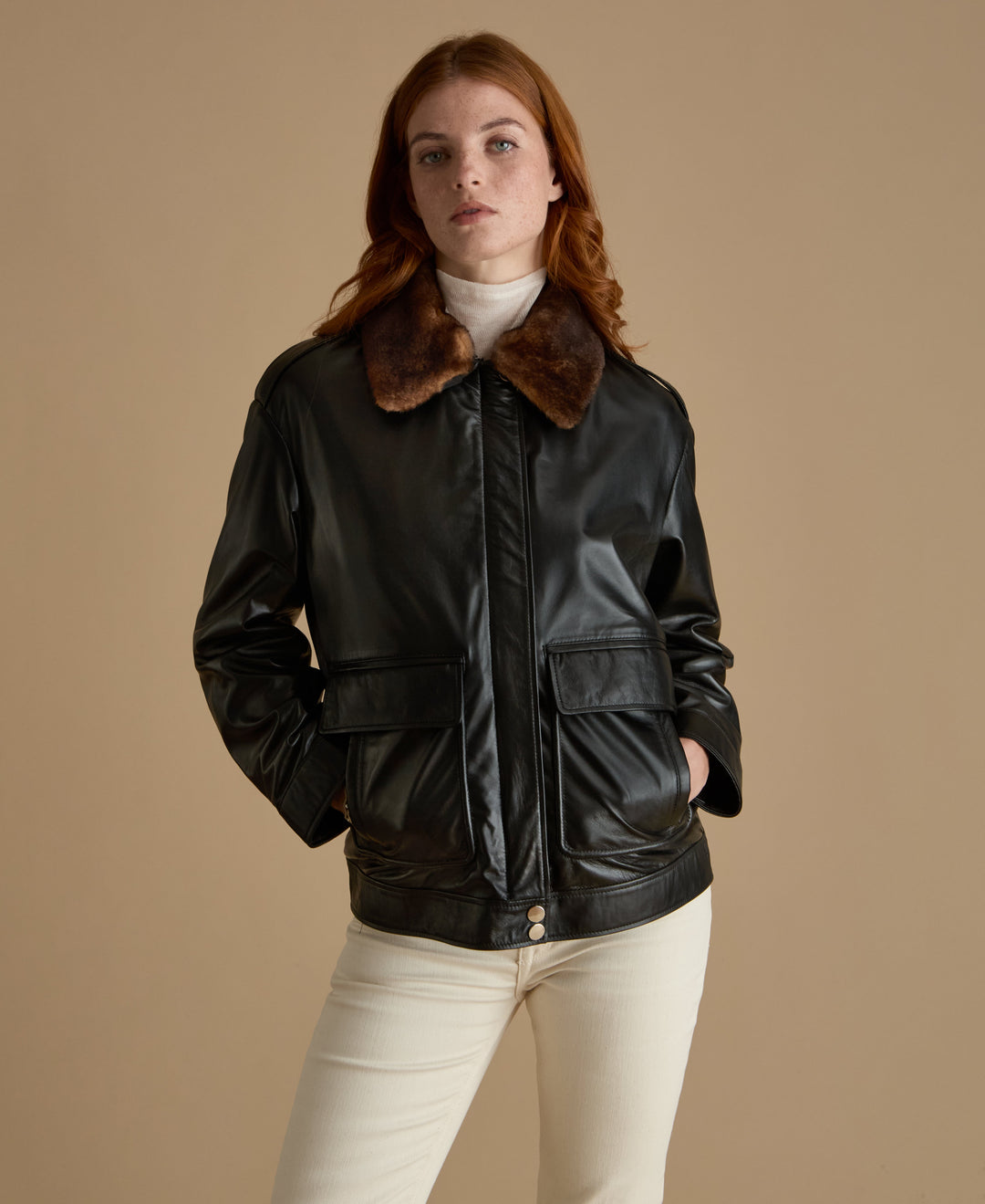 Woman wearing black leather jacket with brown shearling collar, styled with cream trousers – FURNIQ UK women’s leather outerwear