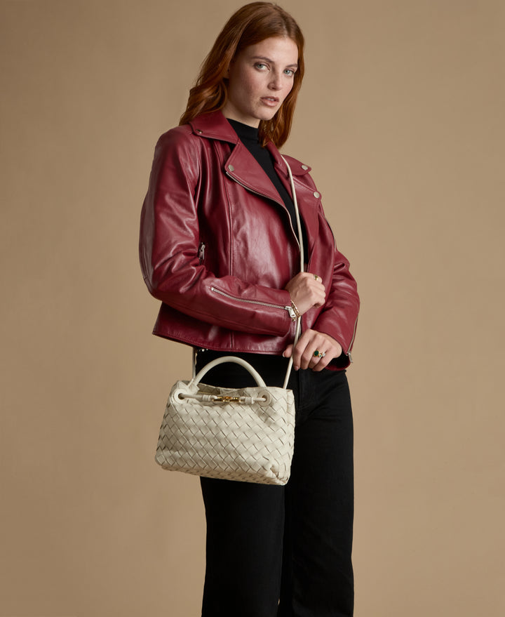 Woman wearing a red leather jacket holding a woven handbag against a beige background