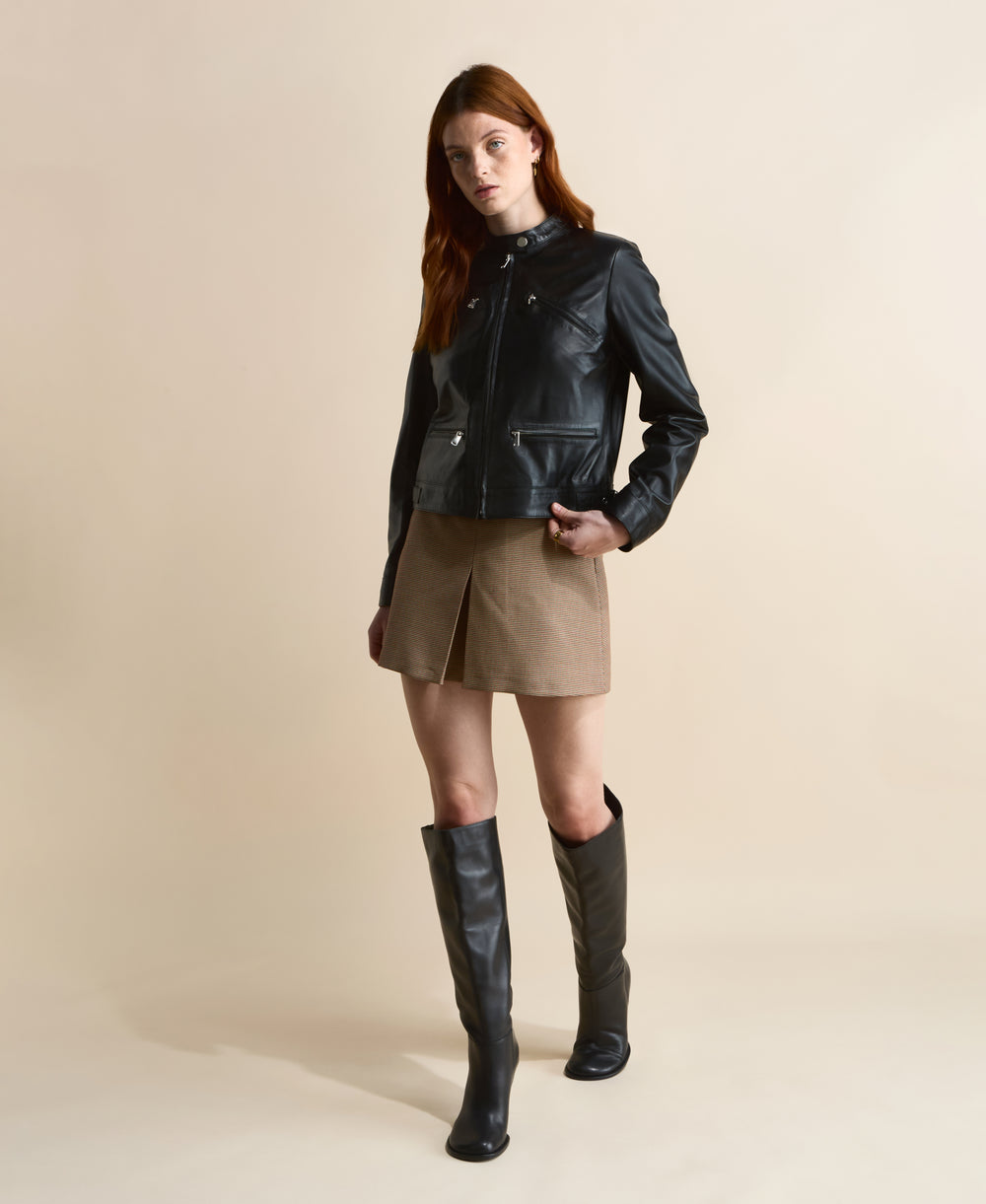 Black leather jacket with zip details styled with brown mini skirt and knee-high black boots, full body front view