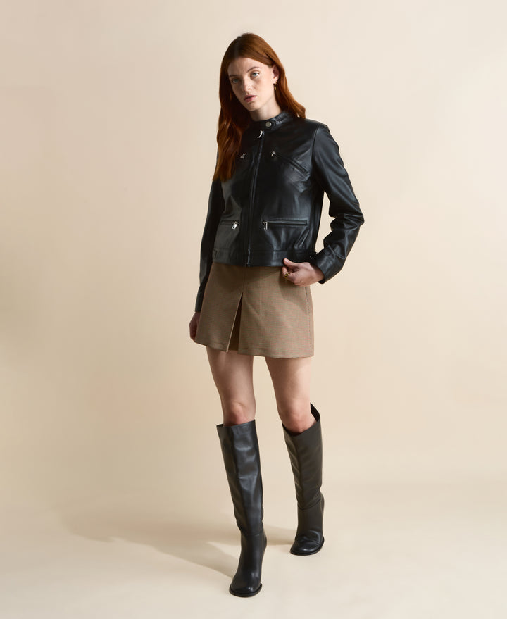 Black leather jacket with zip details styled with brown mini skirt and knee-high black boots, full body front view