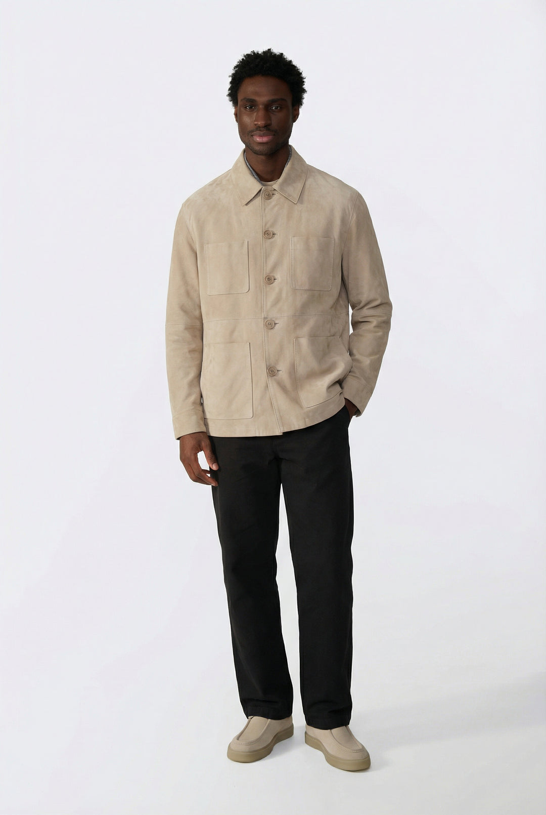 Man wearing a beige suede jacket and black pants on a white background