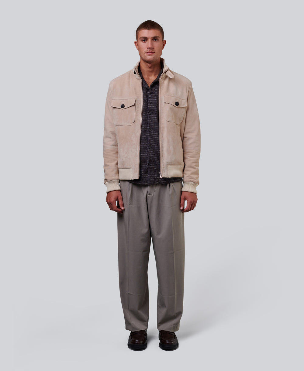 Man wearing a beige suede jacket and gray pants on a white background