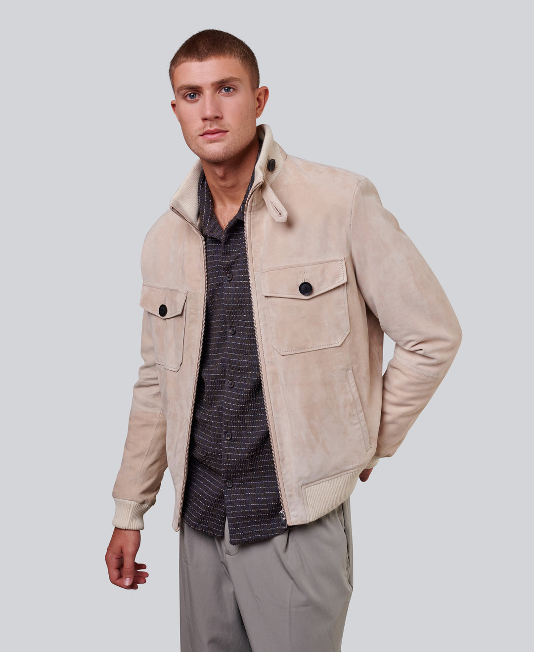 Man wearing a beige suede jacket over a striped shirt on a light gray background