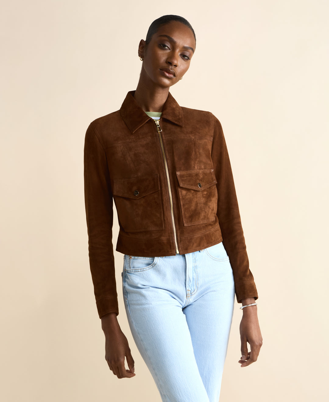 Woman wearing a brown suede jacket and light blue jeans on a beige background