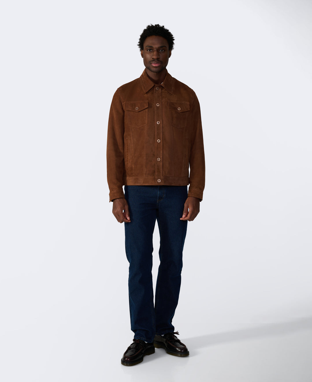 Man wearing a brown suede jacket and dark jeans on a white background