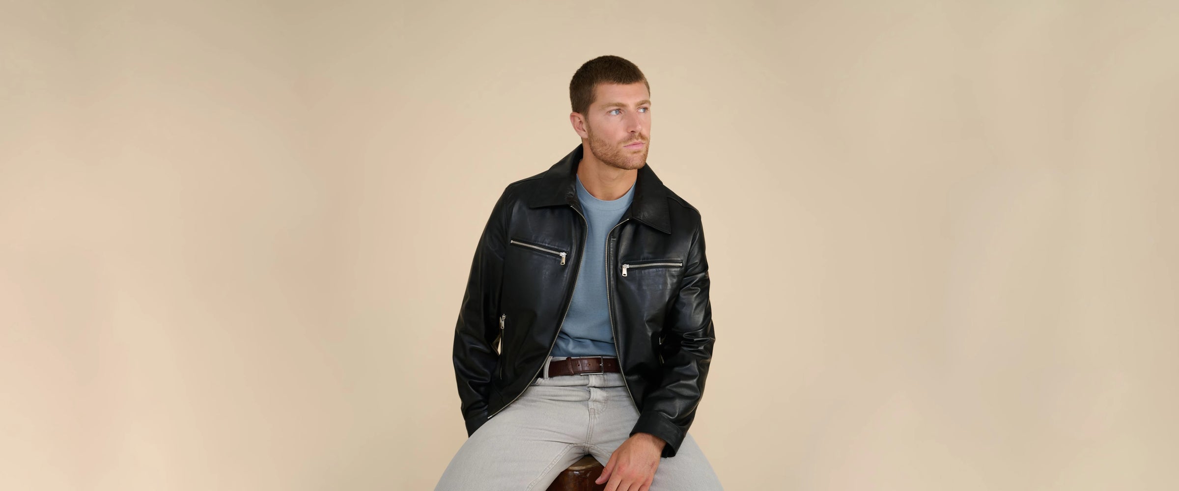 Model wearing black leather jacket with zip pockets styled with blue t-shirt and grey trousers