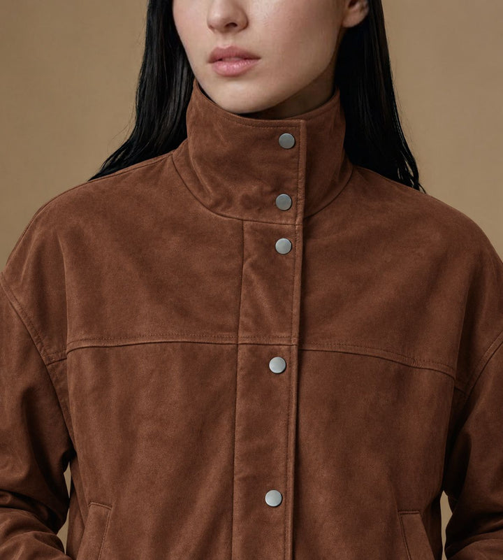 Close-up of the Arden jacket’s chestnut brown suede texture, funnel collar and metal snap fastenings.