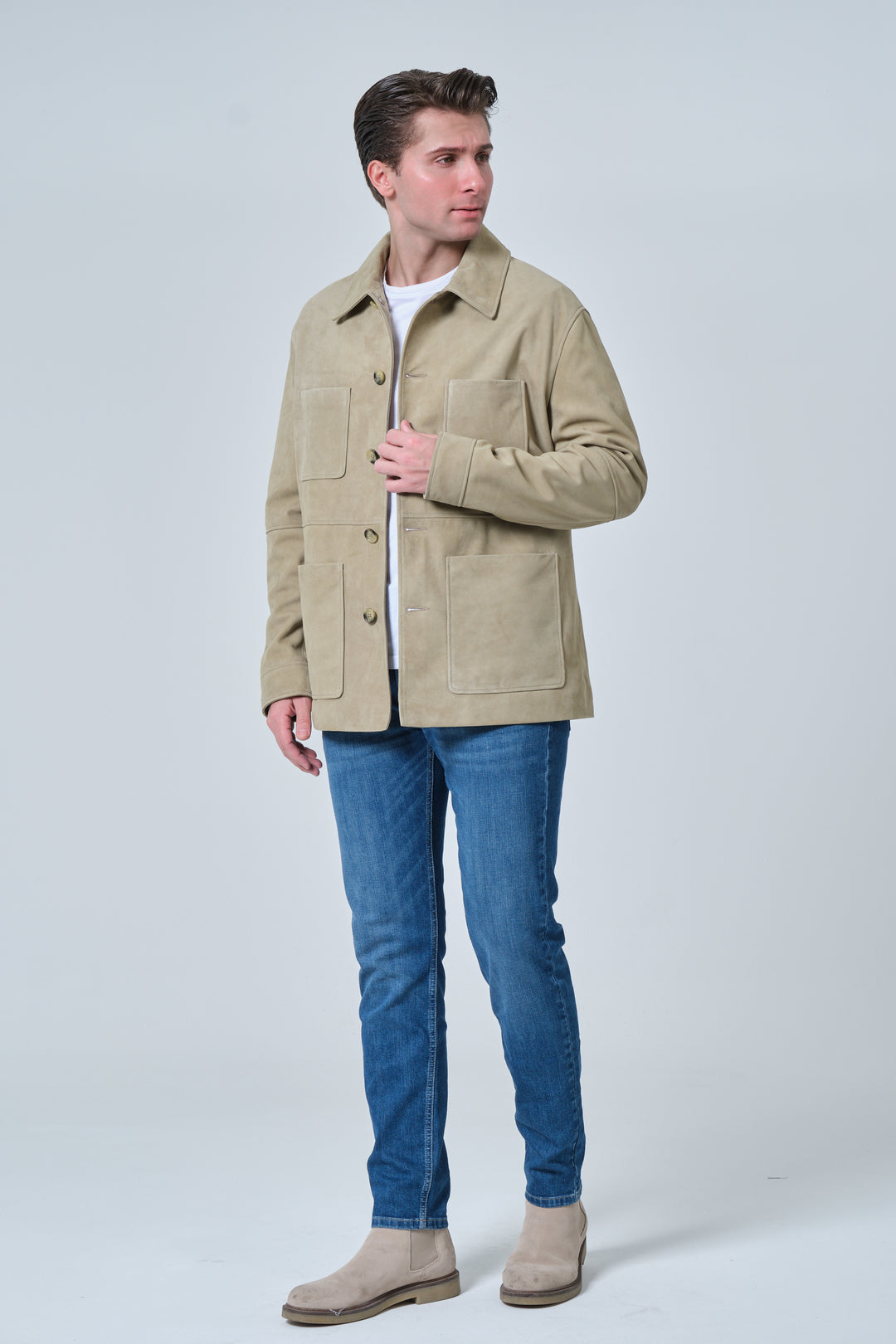 Male model wearing Beckett men's sage green suede chore jacket with blue denim jeans and beige suede boots