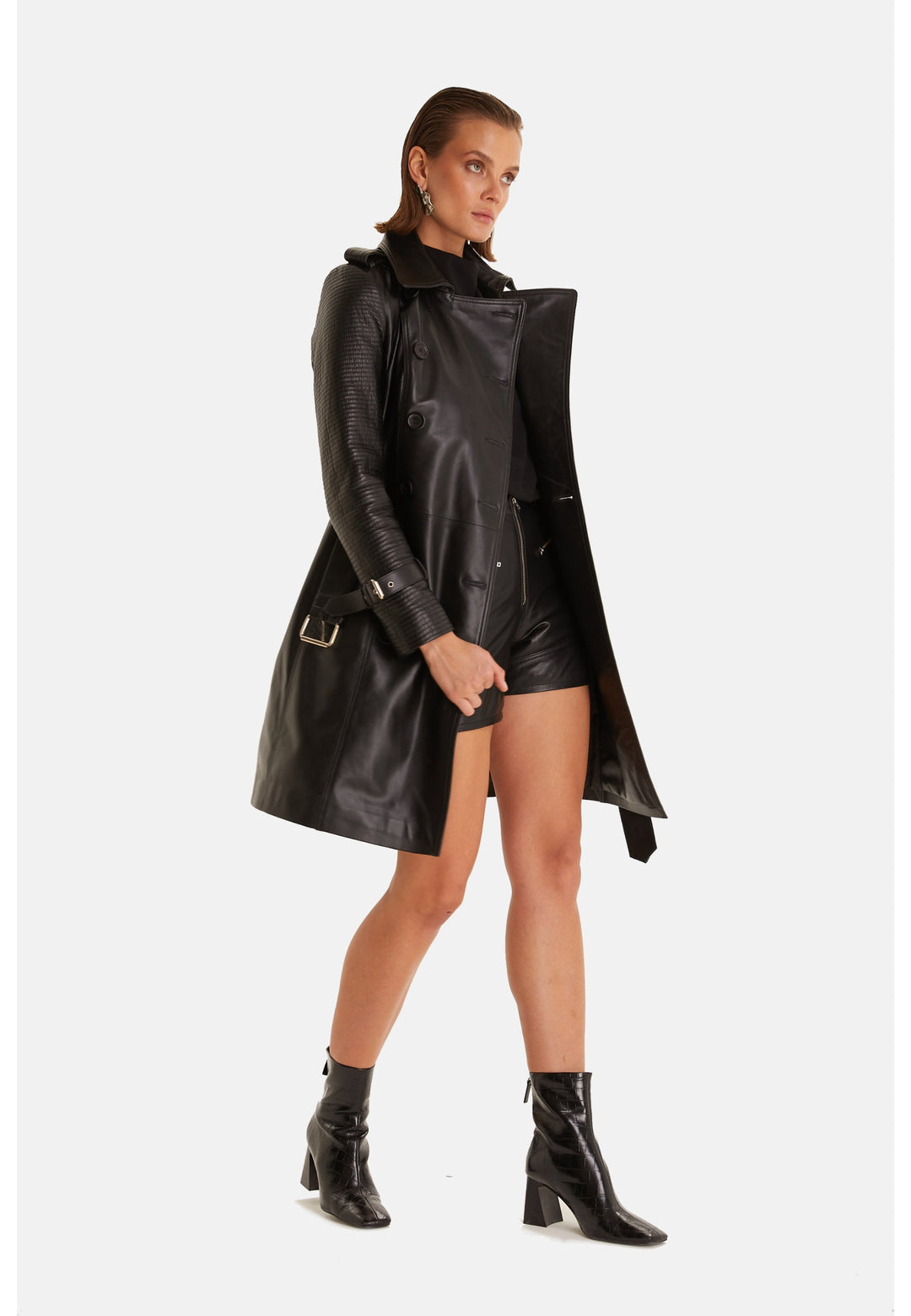 Angled view of the Greenwich black leather trench coat worn open, showing the textured sleeve and above-knee hem.