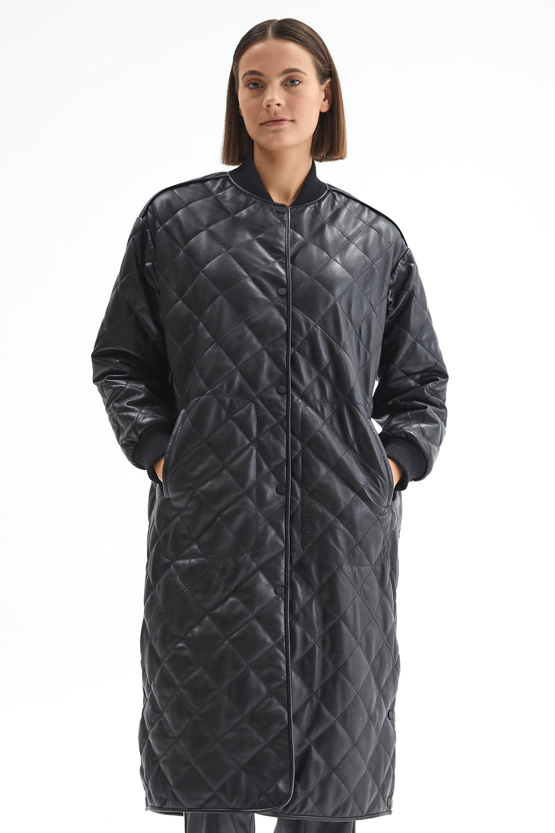Front view of the Kensington black quilted leather coat with snap fastening and hands in the side pockets.