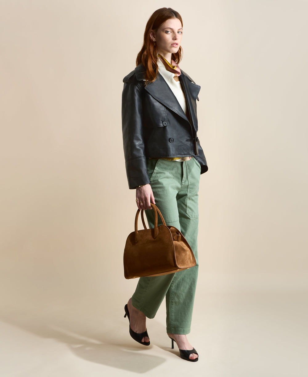 Model wearing the Lola cropped black leather trench coat with green trousers and a brown handbag.