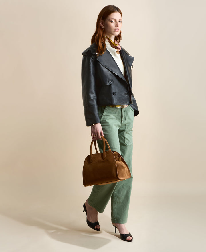 Model wearing the Lola cropped black leather trench coat with green trousers and a brown handbag.