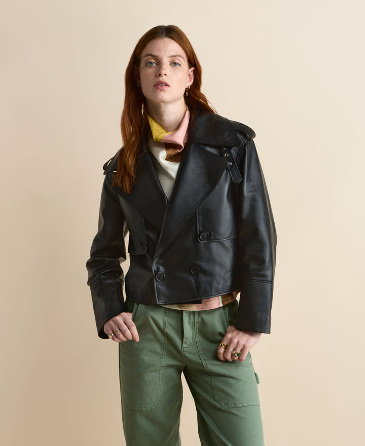 Lola black leather cropped trench jacket shown on a model with wide lapels and double-breasted buttons.