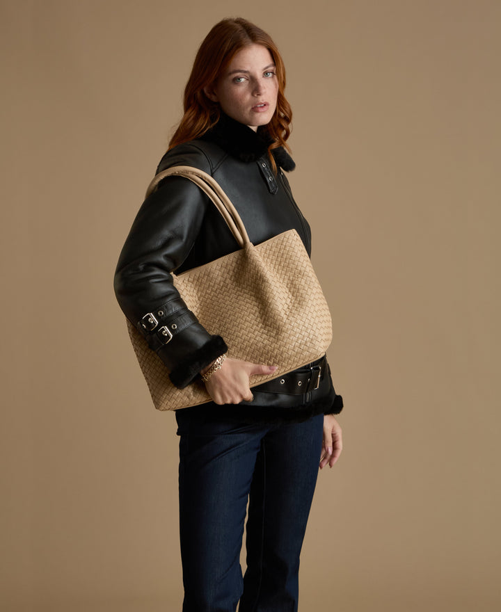 Woman wearing black shearling jacket with cream handbag